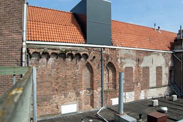 <p>Achtergevel van de voormalige 14e eeuwse ziekenzaal aan de Gasthuisstraat. In deze gevel zijn de bouwsporen te zien van een aantal grote spitsboogvensters. Het boogfries aan de linkerzijde met daarop de restanten van een goot van Drachenfels trachiet heeft bij een nu verdwenen huis behoord. </p>
